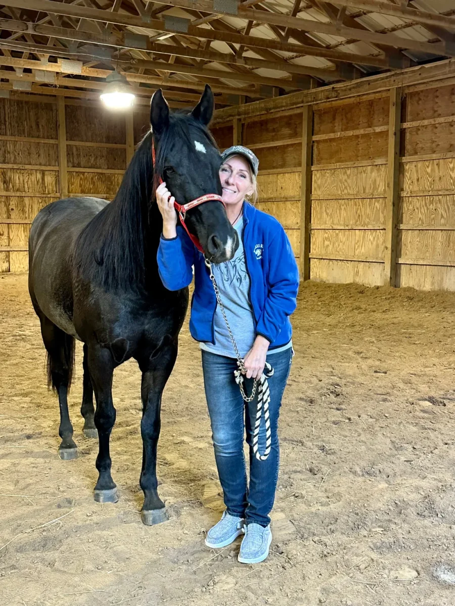 Jean Storie standing with her black horse in an indoor arena