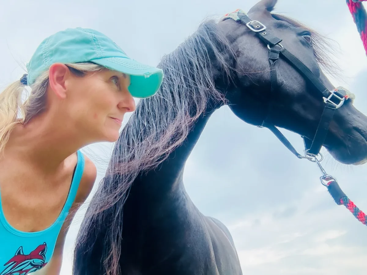 Jean Storie in a teal cap beside her black horse